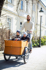 Happy father with two children riding cargo bike in the city