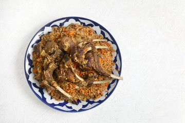 Rice pilaf with lamb ribs , in a traditional dish with ornaments , on a light background . copy space .