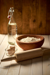 Top view of bowl of flour with yeast and rolling pin on  white  kitchen table