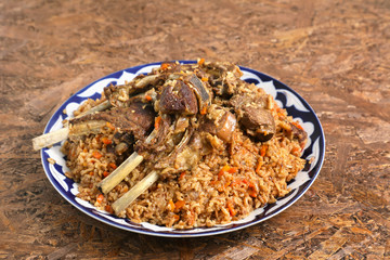 Rice pilaf with lamb ribs , in a traditional dish with ornaments , on a brown textured background .