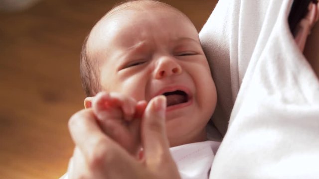 babyhood, motherhood and people concept - mother holding crying baby girl