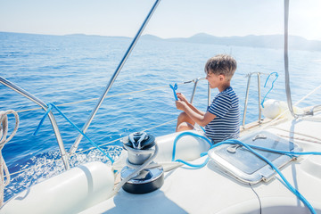 Little boy on board of sailing yacht on summer cruise. Travel adventure, yachting with child on family vacation.