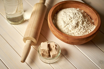 Top view of bowl of flour with yeast and rolling pin on  white  kitchen table