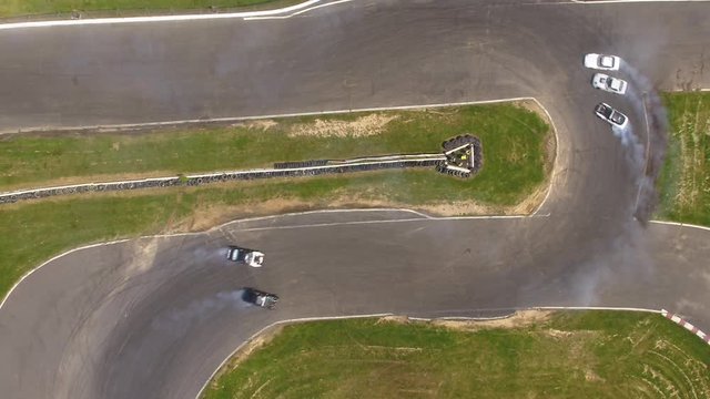 Cars drift around corner on racetrack, overhead aerial