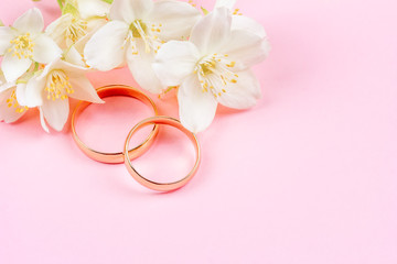pair of gold wedding rings and white Jasmine flowers on pink background with copy space