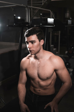 young shirtless fitness man sitting while resting in the gym