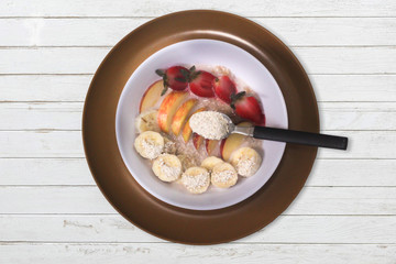 Oat Flakes with sliced bananas and honey, apples and strawberries in bowl. Wood background. Top view.