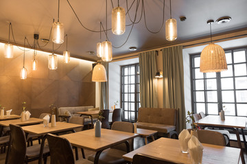 Stylish lamp shining over small tables and comfortable chairs in cozy restaurant