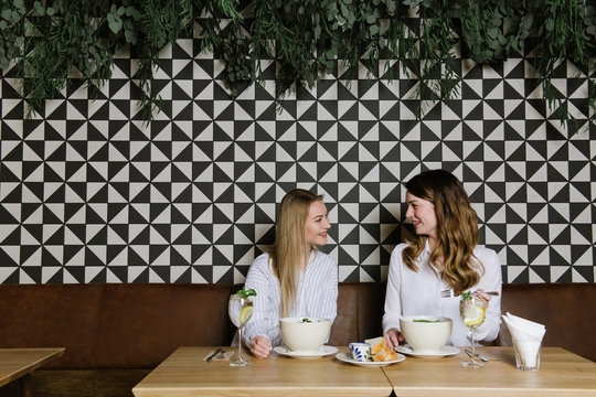 Two pretty ladies smiling and having healthy lunch in cozy restaurant together