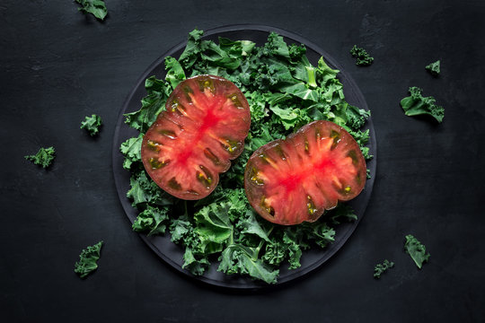 Slices of fresh tomatoes and torn lettuce leaves placed on plate against black plaster background