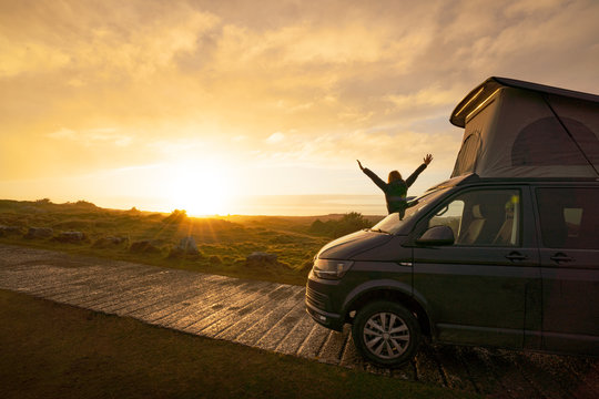 Man silhouette with opening hands while standing on caravan trailer on lonely country road at sunset in Wales