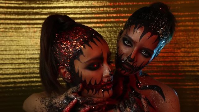 Two young girls models with glitter on their bodies in the role of demons on a golden background. Mystic and Halloween.