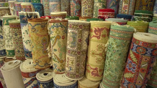 Many different colorful rolled up carpets standing at sore ready for selling. Real time 4k video footage.