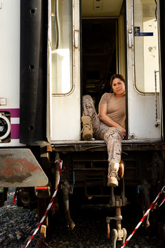 Strong female soldier looking at camera and thinking while sitting in doorway of grungy military vehicle in countryside