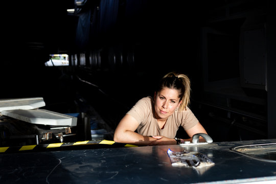 Attractive female soldier looking at camera while sitting inside dark hangar