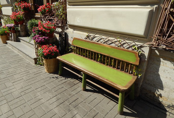 Old vintage green cozy empty wooden bench on the street, and next to a basket of flowers