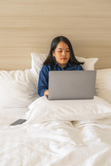 Woman using laptop put on white pillow inside bedroom