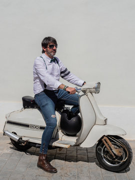 Positive middle-aged hipster in elegant clothes with retro motorbikes looking away in sunny day
