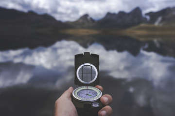 Hand of anonymous traveler holding compass against tranquil mountain lake on cloudy day in Spanish countryside