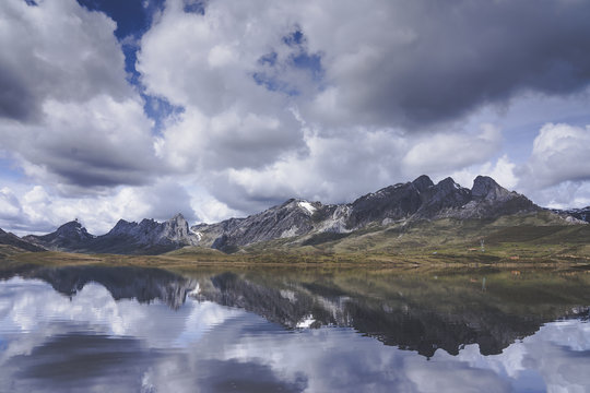 Thick white clouds floating over mountain ridge and calm surface of Embalse del Casares lake in Leon, Spain