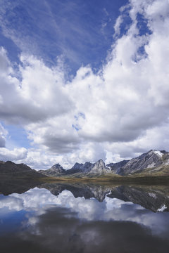 Thick white clouds floating over mountain ridge and calm surface of Embalse del Casares lake in Leon, Spain