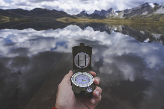 Hand of anonymous traveler holding compass against tranquil mountain lake on cloudy day in Spanish countryside