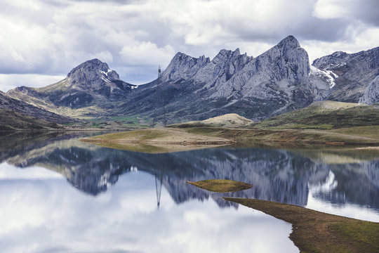 Thick white clouds floating over mountain ridge and calm surface of Embalse del Casares lake in Leon, Spain