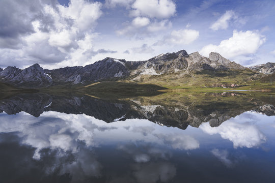Thick white clouds floating over mountain ridge and calm surface of Embalse del Casares lake in Leon, Spain