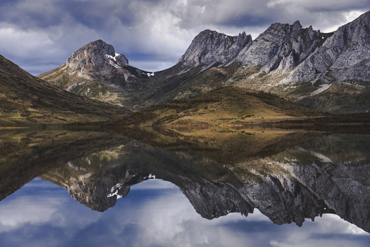 Thick white clouds floating over mountain ridge and calm surface of Embalse del Casares lake in Leon, Spain