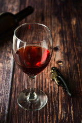 Glass of red wine over rustic, wooden textured table. Dark photo.