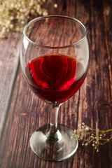 Glass of red wine over rustic, wooden textured table. Dark photo.