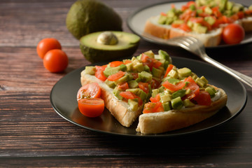 Healthy toast with avocado, cherry tomatoes and cheese on a plate. Wooden table.