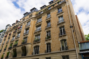 Fototapeta na wymiar Building with large windows and balconies with flowers in Paris against a cloudy sky
