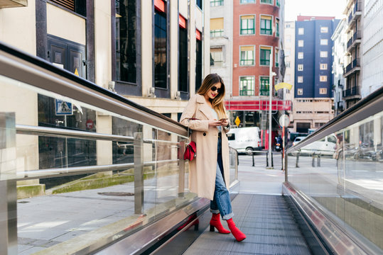 Young cheerful female leaning on stairs with smartphone