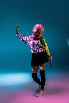 Young Asian woman with stylish pink haircut and sparkly silver jacket standing and listening music