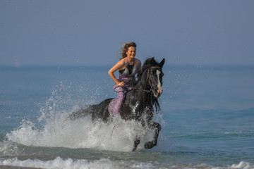 Portrait of a beautiful blond girl galloping on horseback, dissecting waves on the sea beach