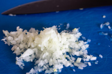 Chopped onions on the Board with a black knife. Finely chopped onion on a Board with a black knife. Finely chopped onion on a blue Board. Finely chopped onion with black knife