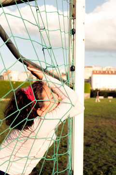 Young girl leaning on a football goal net, tired afyer playing soccer with friends
