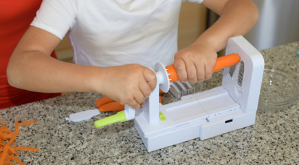 Child preparing lunch. Putting carrots in a manual machine