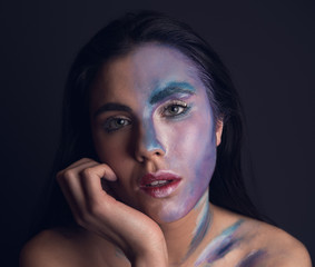 Young attractive woman with painting blue and silver color face on black background looking at camera