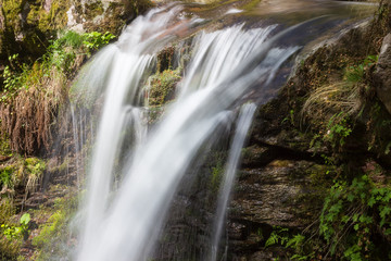 Close up, artistic view from above of a powerful waterfall cascades streaming down the wet, red rocky cliff covered by moss