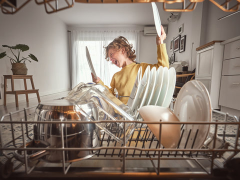 Little boy with wavy hair yawning while standing near open dishwasher in early morning in kitchen