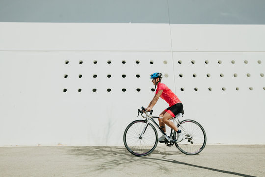 Female in helmet and sportswear riding bike on city street on sunny day
