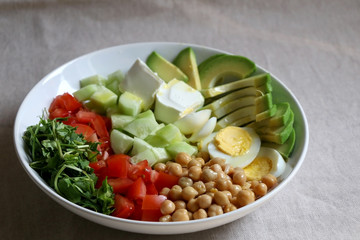 Lunch bowl with avocado, hard boiled egg, chickpea, feta cheese, cucumber, tomato and arugula. Selective focus.