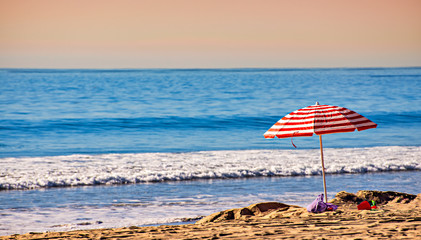 Panoramic California beach scene with colorful beach umbrella next to the ocean; selective focus.