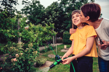 Mother embracing and kissing daughter while she watering garden