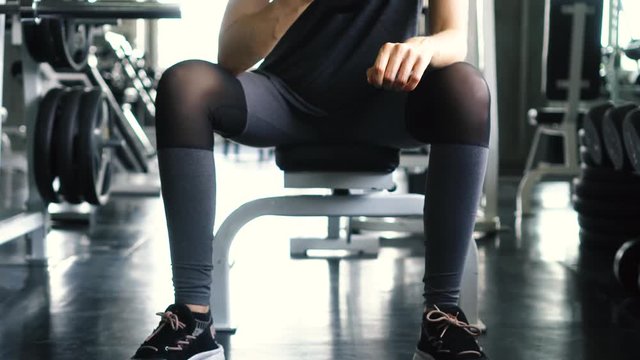 Young woman in sportswear doing seated dumbbell concentration curl bicep exercise at the gym