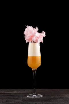 Closeup vertical glass of yellow layered cocktail decorated with cotton candy at black isolated background.