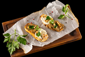 Italian bruschetta with cream cheese, nuts and meat paste at wooden board isolated at black background.