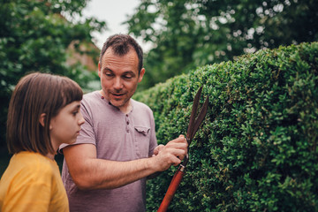 Father teaching daughter to prune hedge